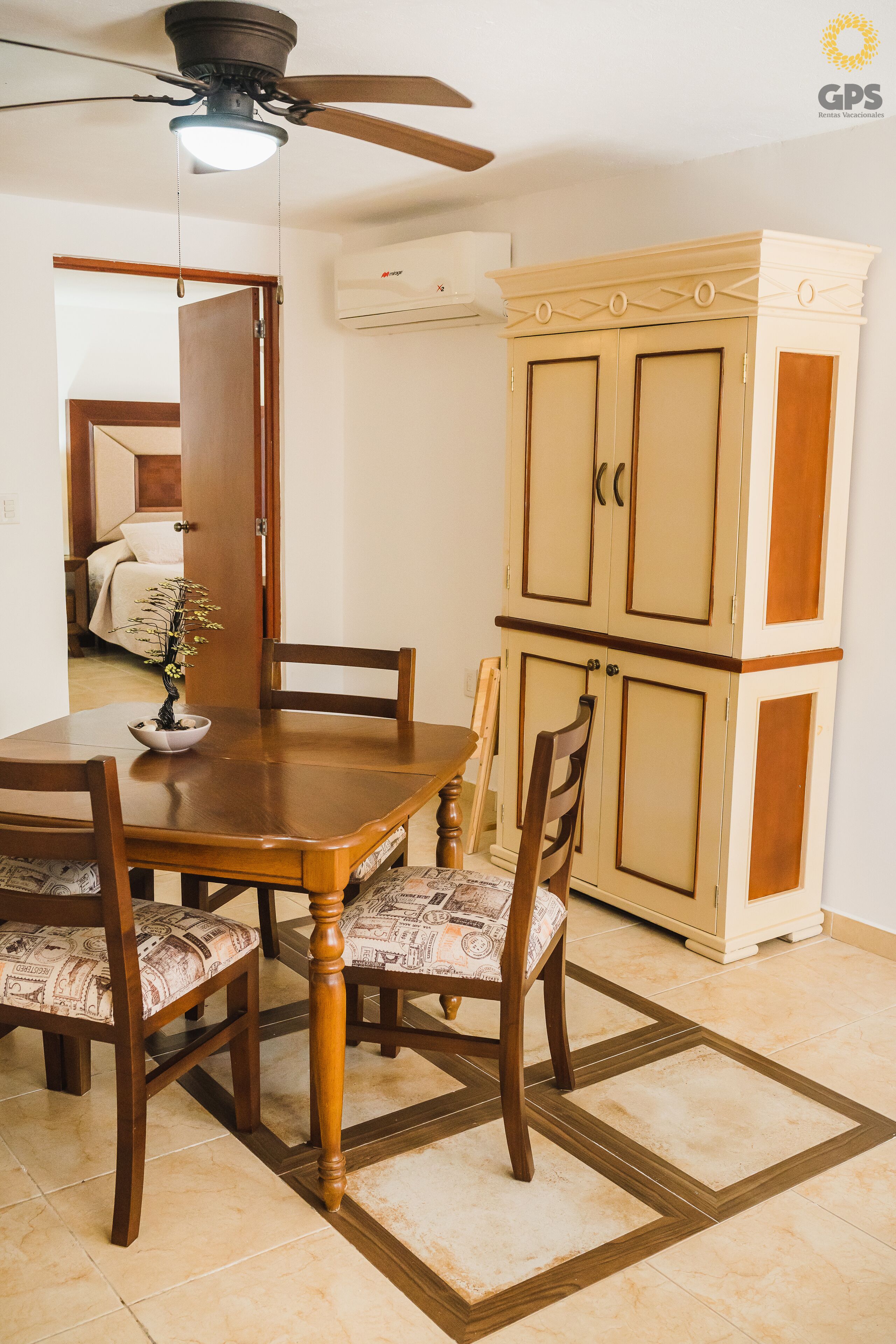 Un comedor con una mesa y sillas de madera, un ventilador de techo y un armario con dos puertas.