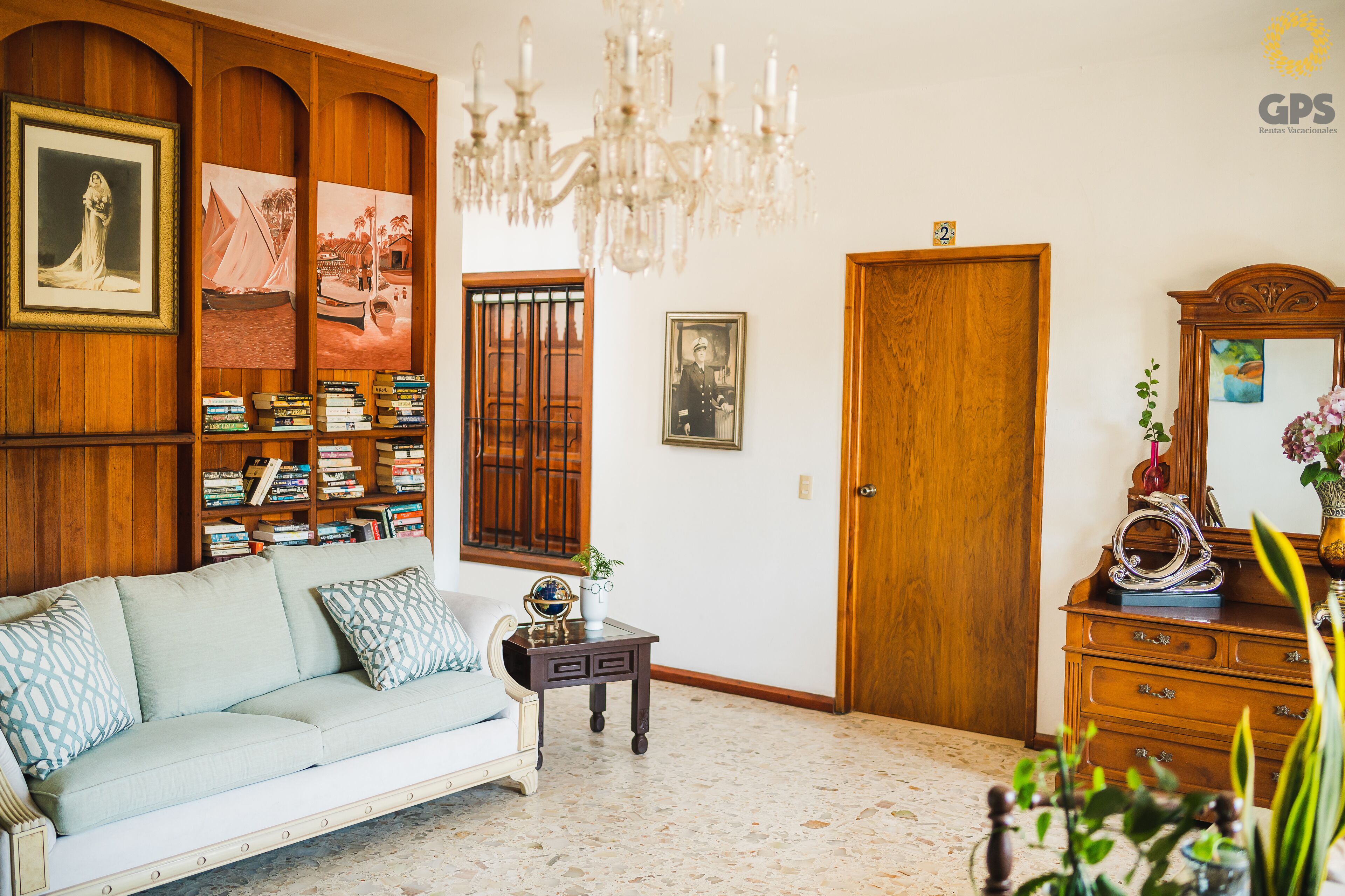 Una habitación con una estantería de madera, un sofá blanco, un armario de madera y una araña.