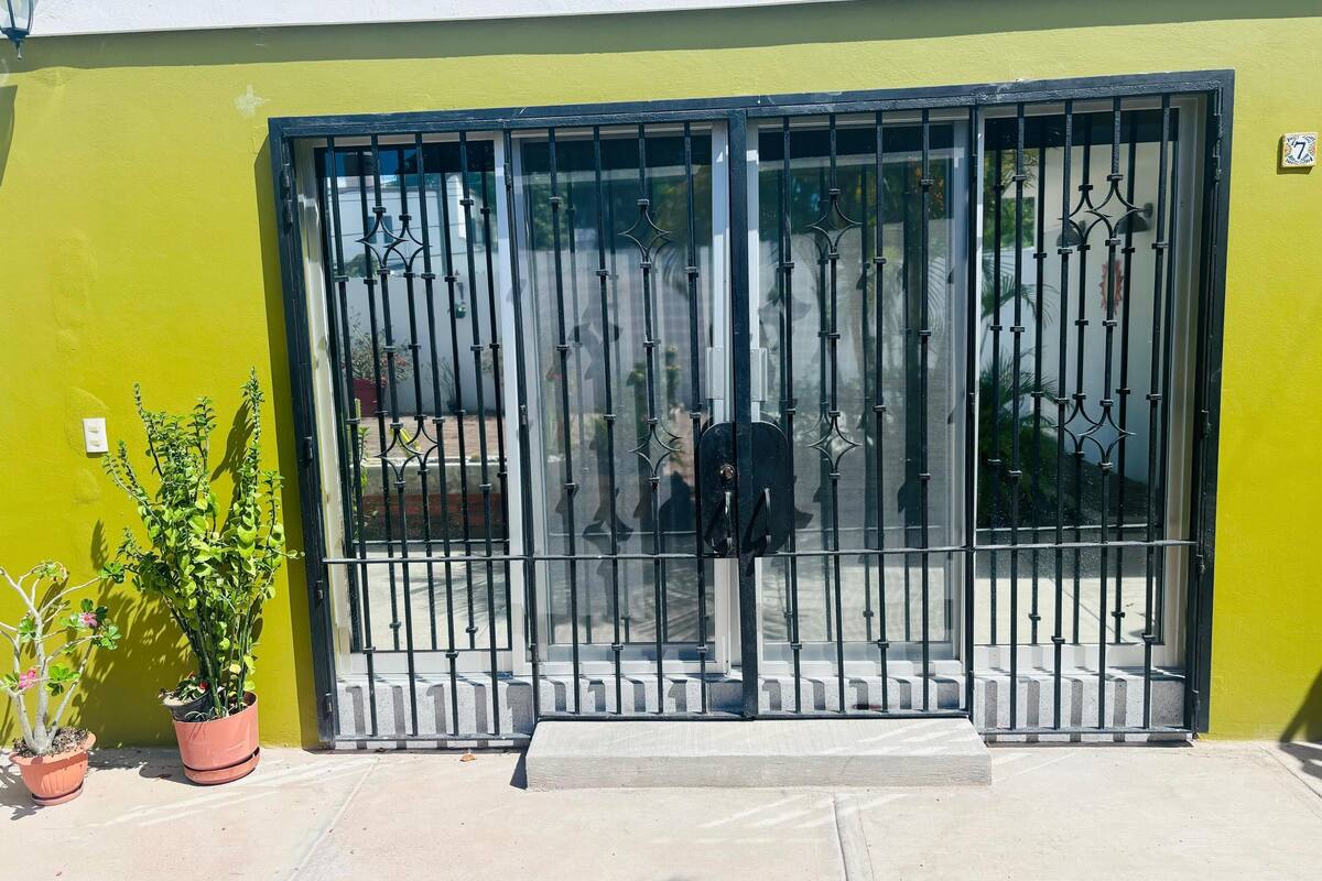 Um edifício amarelo com portão de metal e plantas em vasos.