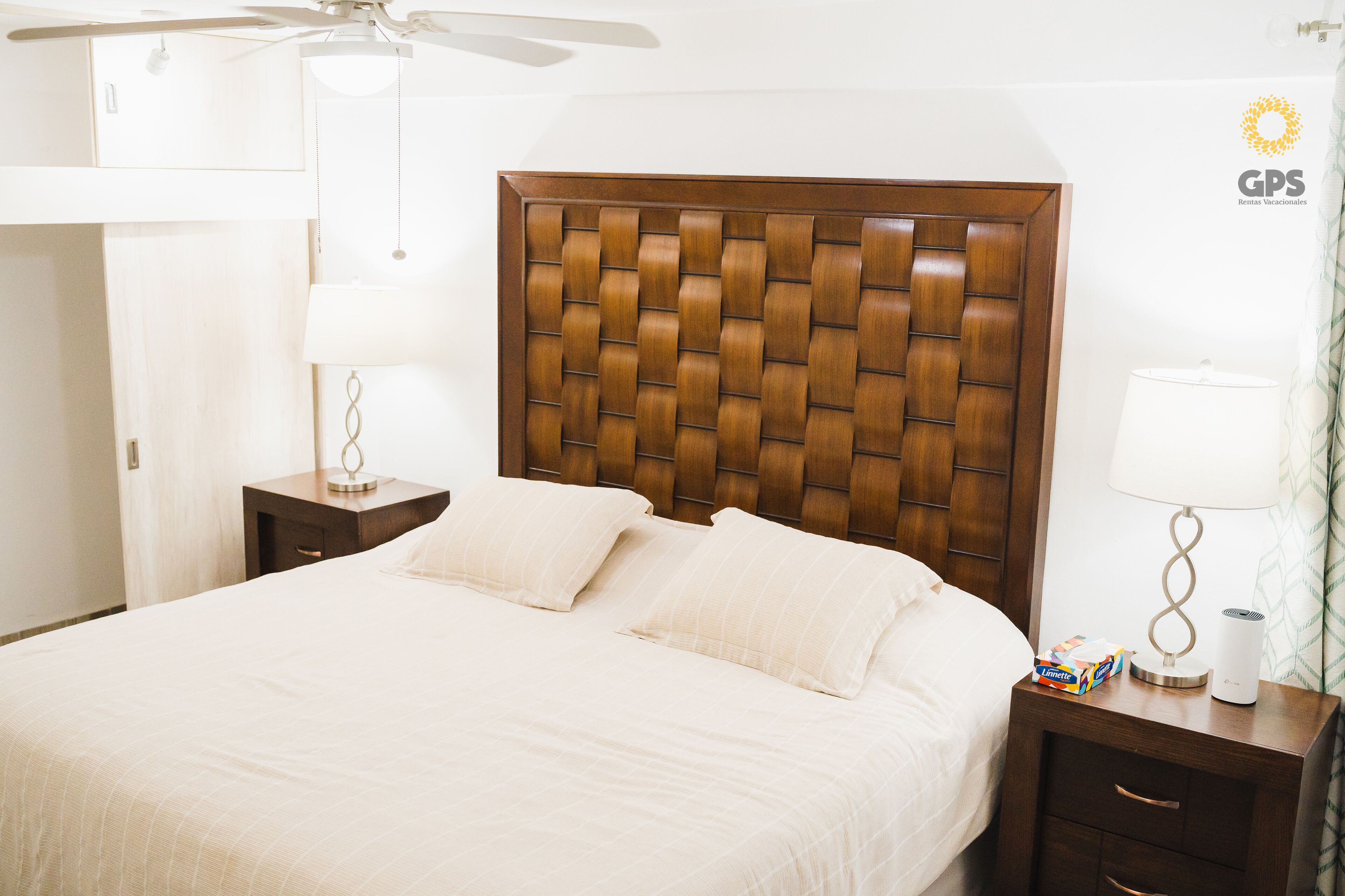 A hotel room with a large bed, wooden headboard, bedside tables, lamps, and a ceiling fan.