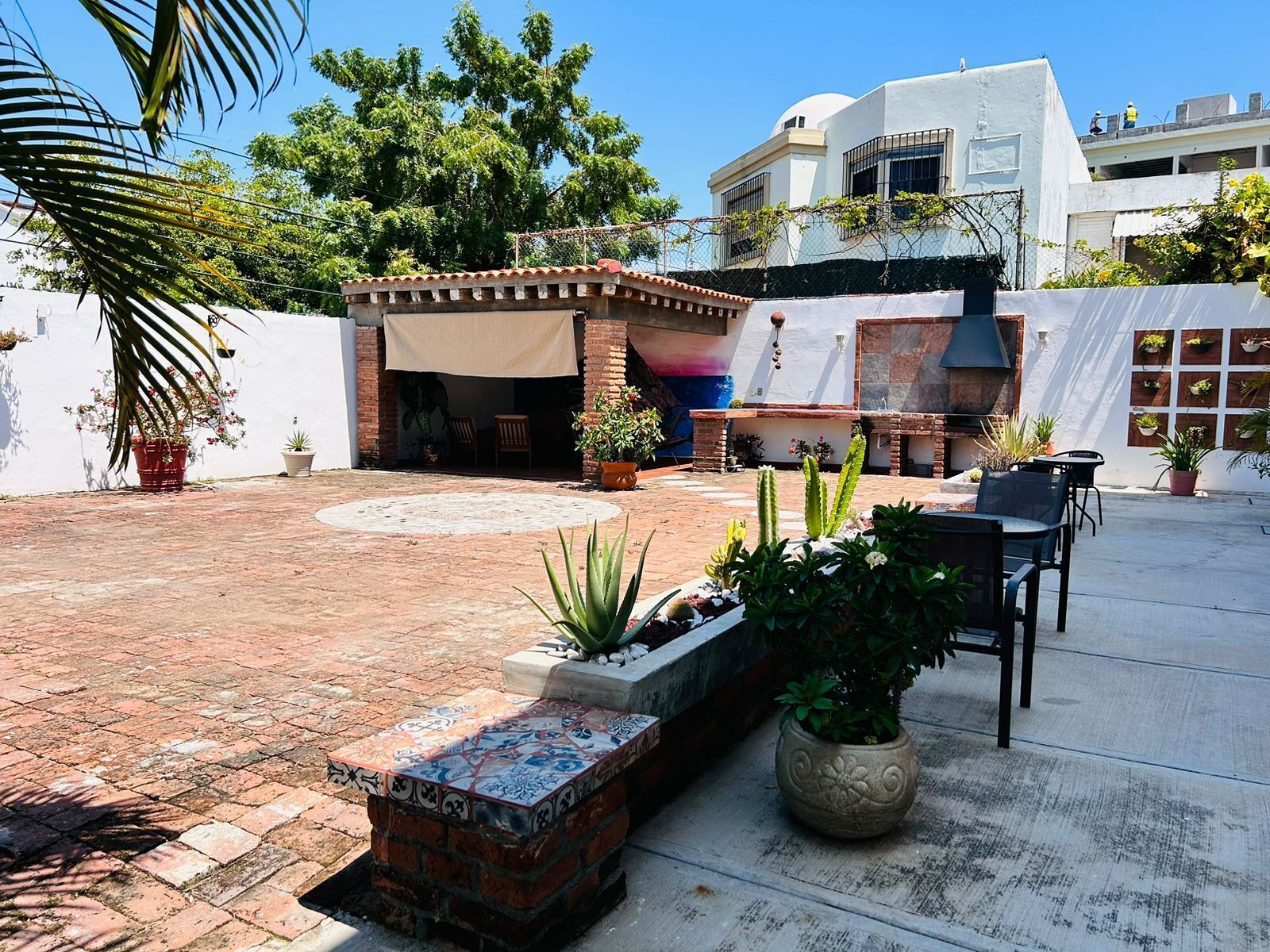 A patio area with a brick floor, outdoor seating, potted plants, and a pergola with a canopy.