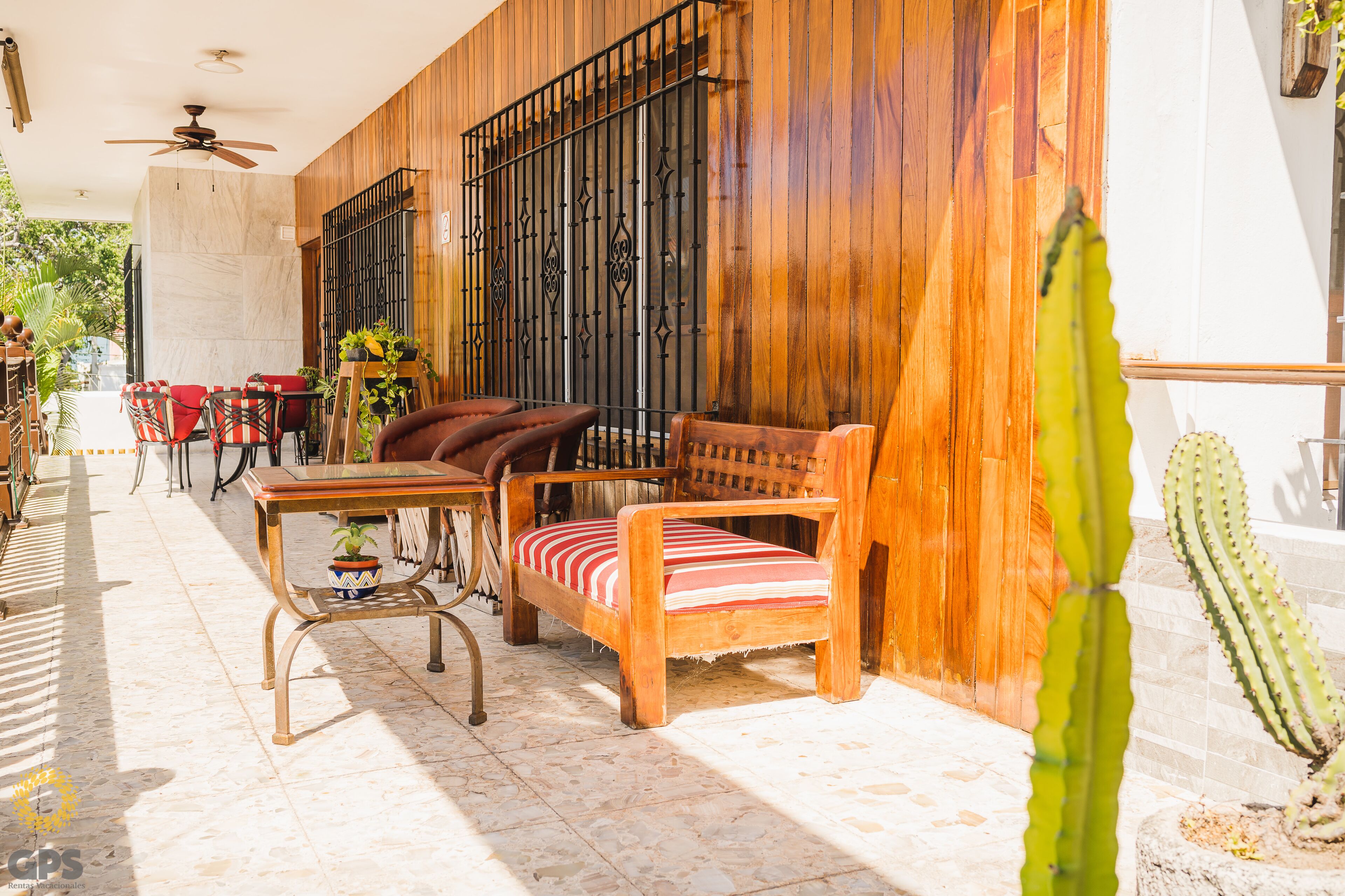 Eine Terrasse mit Holzmöbeln, einem Deckenventilator und einer Kakteenpflanze.