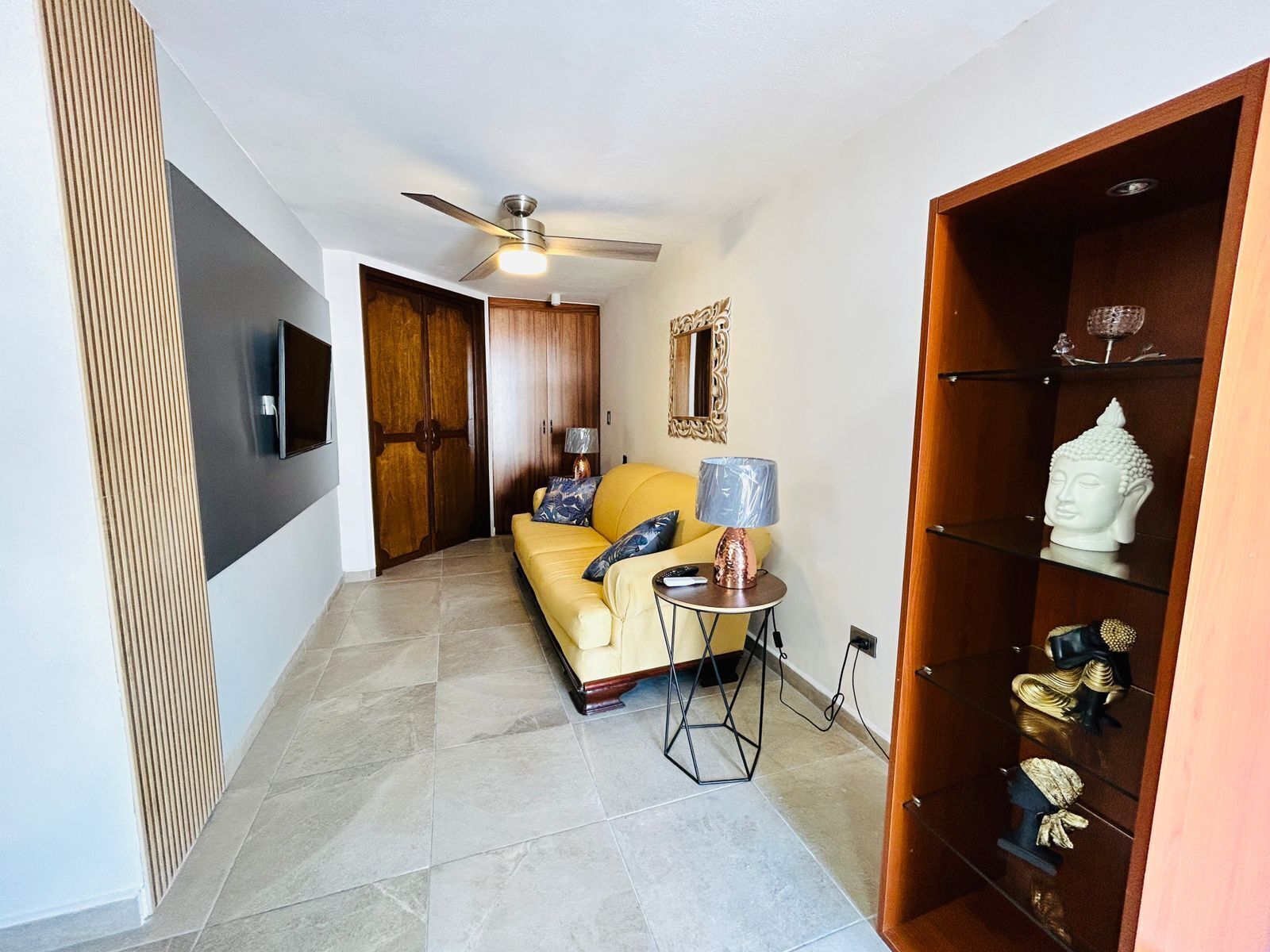 A modern living room with a sofa, a small side table, a ceiling fan, and a wooden cabinet with decorative items.