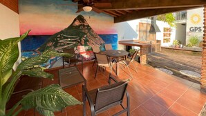 An outdoor patio with a mural of a mountain and sunset, wooden ceiling beams, and a table with chairs. - Meson del Capitan Apartments (Mazatlán)