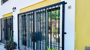 A building with a yellow and white facade, black metal gates, and a potted plant in the foreground. - Meson del Capitan Apartments (Mazatlán)