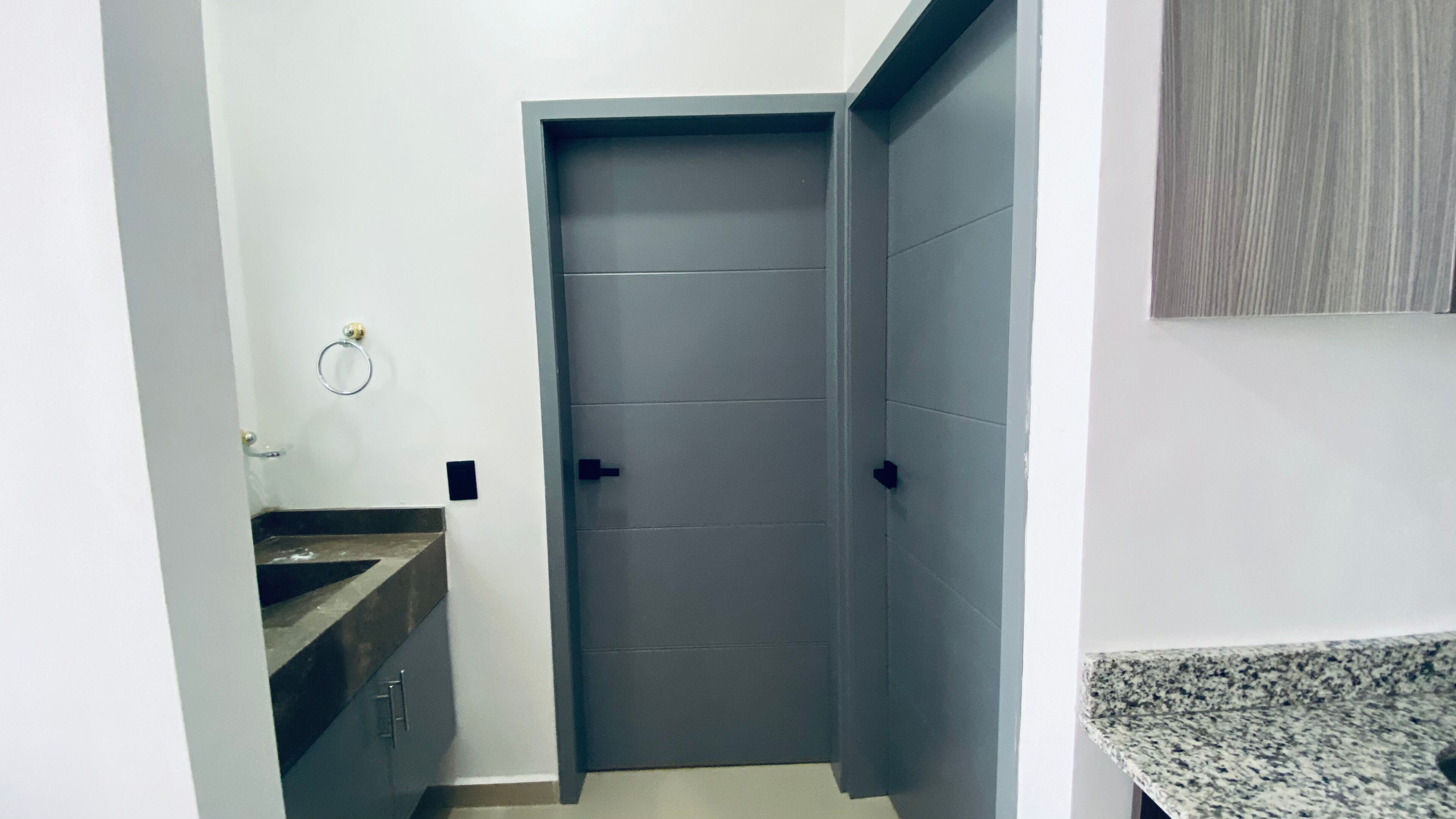 A bathroom with a dark door, a sink with a marble countertop, and a towel ring on the wall.