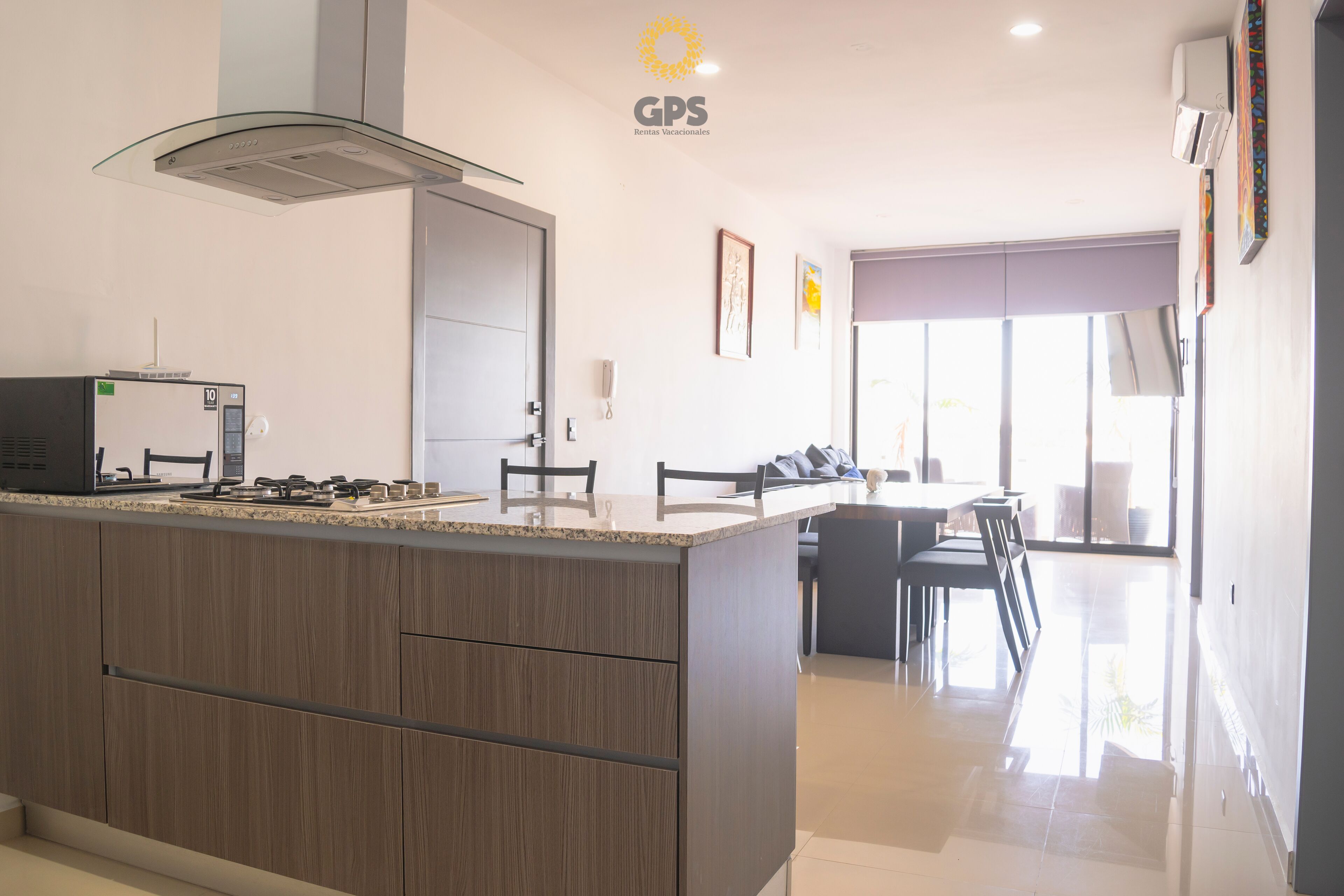 A modern kitchen with a central island, a dining area with chairs, and a large window providing natural light.