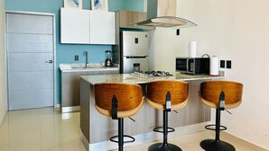 Una cocina moderna con barra, que incluye una isla central con taburetes, microondas, cocina a gas y pileta.