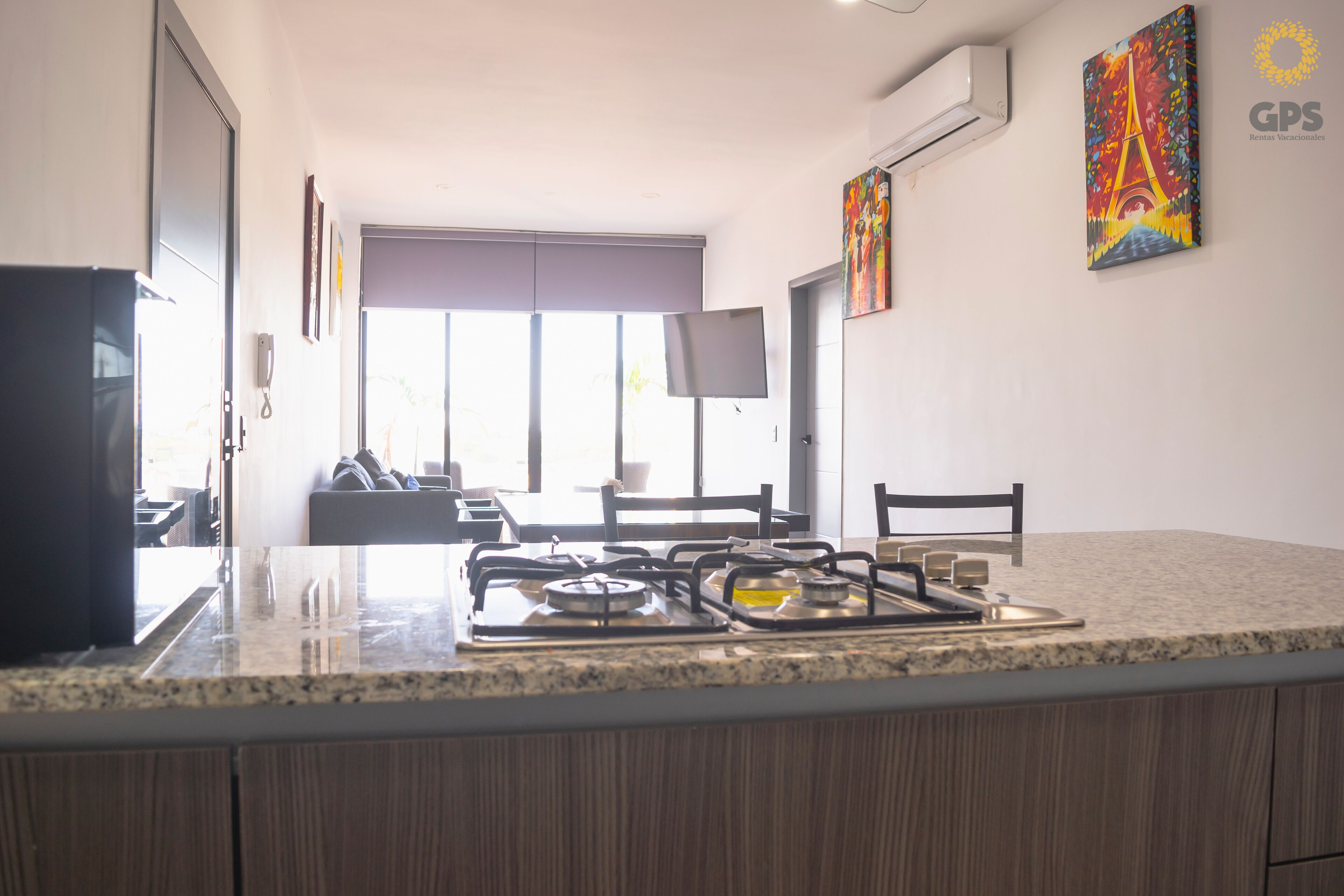 A modern kitchen with a gas stove, a flat-screen TV mounted on the wall, and a painting of the Eiffel Tower.