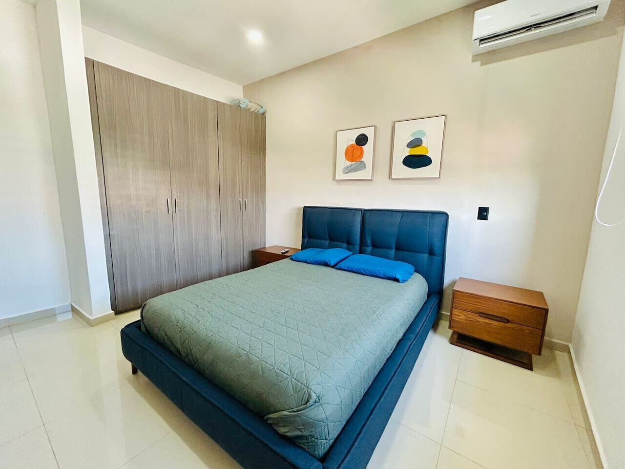 A bedroom with a bed, a nightstand, a wardrobe, and two wall art pieces.