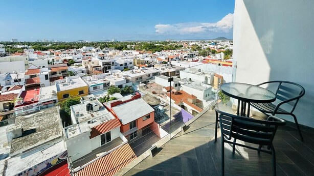 Un balcón con mesa y sillas que da a una zona residencial con varios edificios y un cielo despejado.