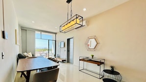 Una sala de estar moderna con una mesa de comedor, sillas, un sofá y una mesa de centro. Hay un ventanal que ofrece vistas al exterior.