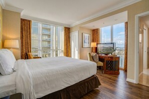 Habitación de hotel con una cama grande, un escritorio con televisor y vistas a la ciudad a través de amplios ventanales.