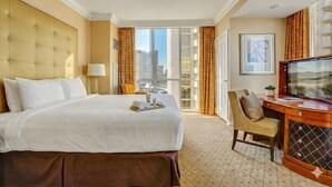 A hotel room with a large bed, a desk with a TV, a window with curtains, and a view of buildings. - MGM Signature | 11th Floor 1BR | Strip View | No Resort Fee (LAS VEGAS)