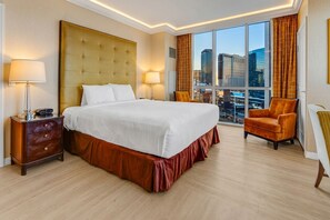 Une chambre d’hôtel avec un grand lit, deux tables de chevet, une chaise et une vue sur le paysage urbain grâce à de grandes fenêtres.