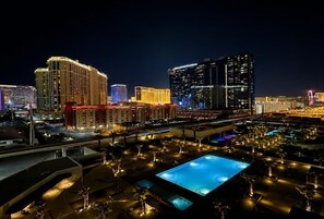 A nighttime cityscape with illuminated buildings, a large pool area, and a well-lit parking structure.