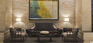 A lobby with a stone wall, a large abstract painting, a dark leather sofa, two armchairs, a small round table, and two lamps on side tables.