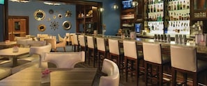 A bar area with multiple seating options including bar stools and tables, a bar counter with a variety of bottles, and a television screen mounted on the wall.
