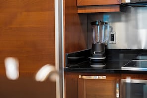 A kitchen with a blender on a black countertop, wooden cabinets, and a stainless steel range hood.