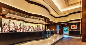 Un hall d’hôtel moderne avec un comptoir d’accueil incurvé, un grand mur orné d’un motif floral rouge et une œuvre d’art encadrée accrochée au mur.