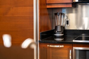 Una cocina con encimera negra, una licuadora, armarios de madera y un electrodoméstico de acero inoxidable.