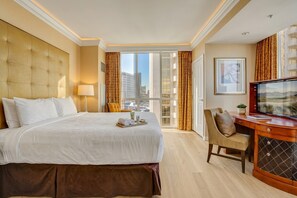 Habitación de hotel con una cama grande, un escritorio con televisor y vistas a la ciudad desde la ventana.
