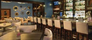 A bar area with multiple seating options, including bar stools and tables, and a variety of bottles and glasses on shelves.