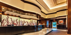A modern hotel lobby with a curved reception desk, a large wall with a red floral pattern, and a framed artwork on the wall. - MGM Signature | 11th Floor Studio | Strip View | No Resort Fee (LAS VEGAS)