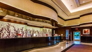 Un moderno hall de hotel con un mostrador de recepción curvo, una gran obra de arte abstracto en la pared y piso de madera.