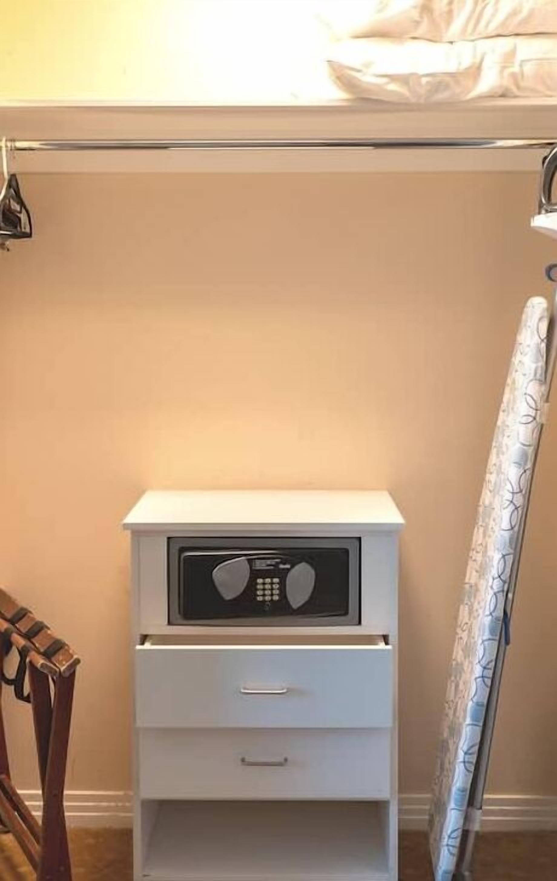 Une table de chevet blanche, avec une radio, un tiroir et un rideau sur le côté droit.