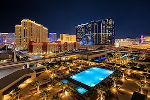 A hotel with multiple swimming pools, a large urban skyline in the background, and a well-lit outdoor area with palm trees. - MGM Signature | 11th Floor Studio | Strip View | No Resort Fee (LAS VEGAS)