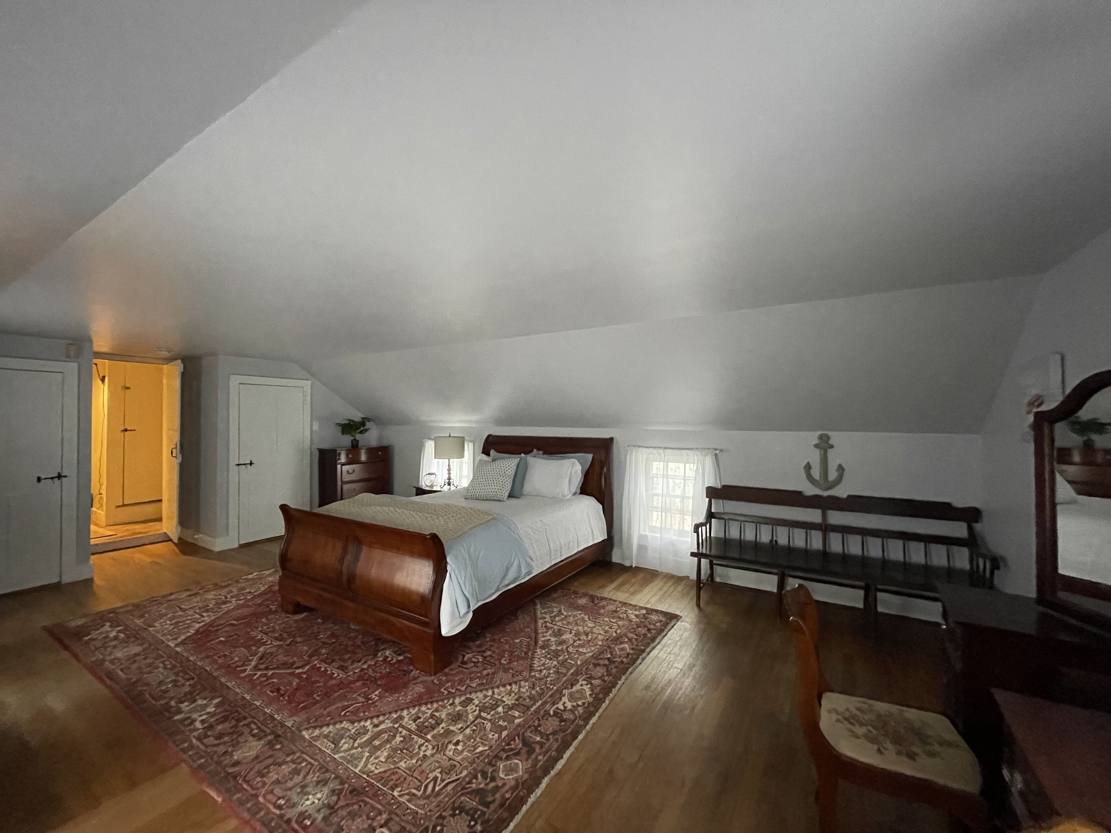 Une chambre à coucher avec un lit en bois, une table de chevet, un bureau, une chaise et une fenêtre avec des rideaux.