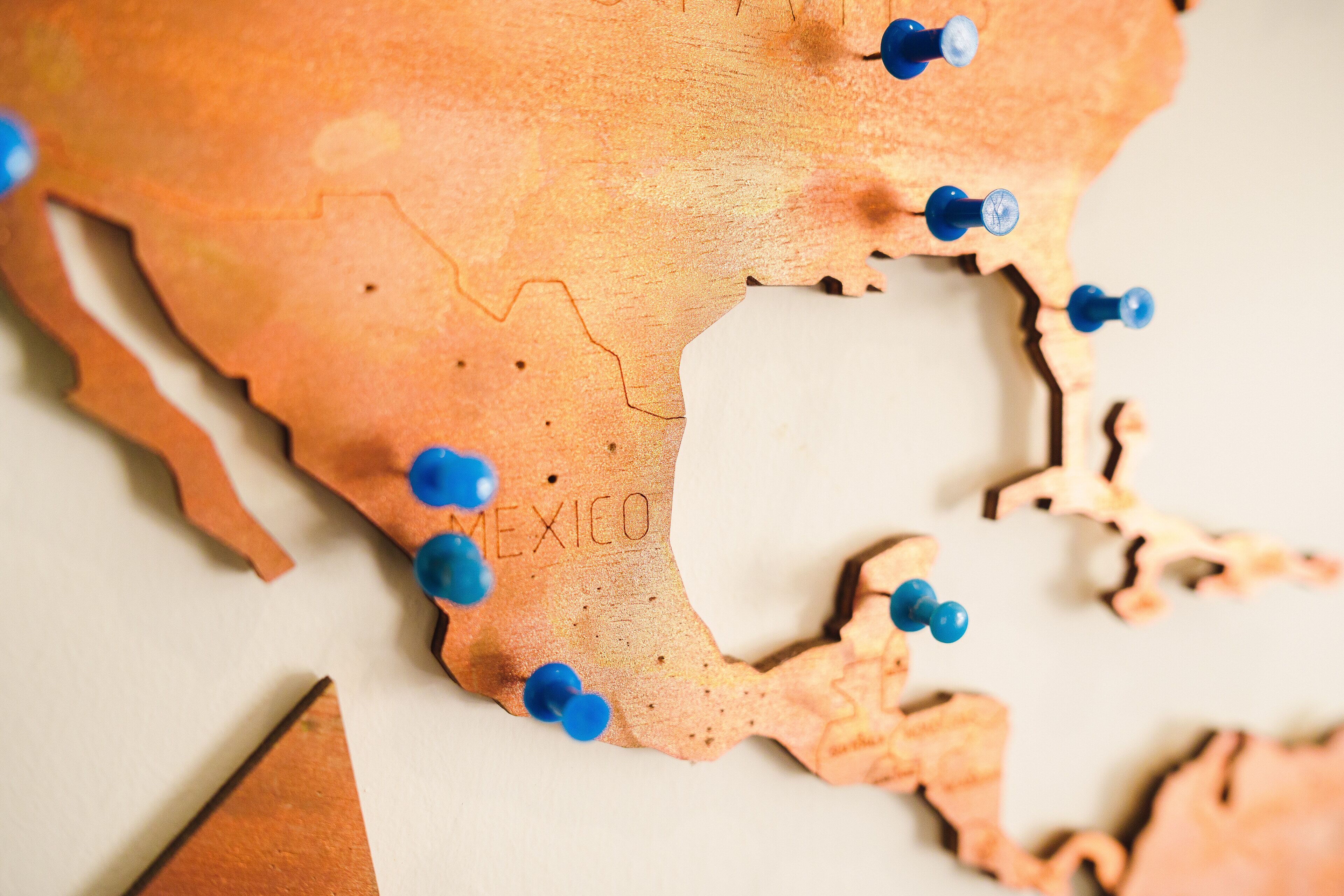 A wooden map with Mexico labeled, featuring blue pins and a triangular cutout.
