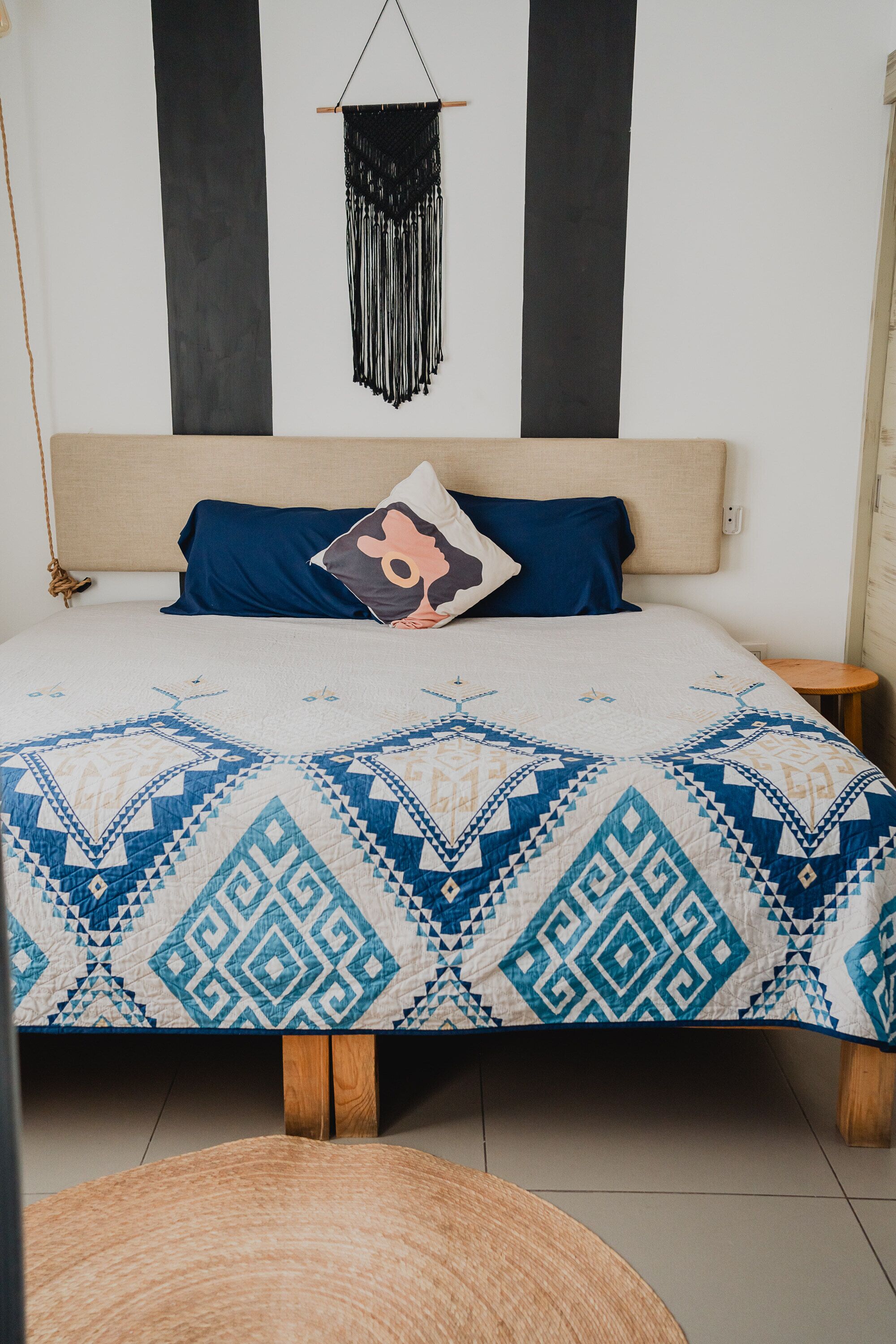 Un letto con una coperta a motivi, una testiera e una decorazione in macramè appesa.