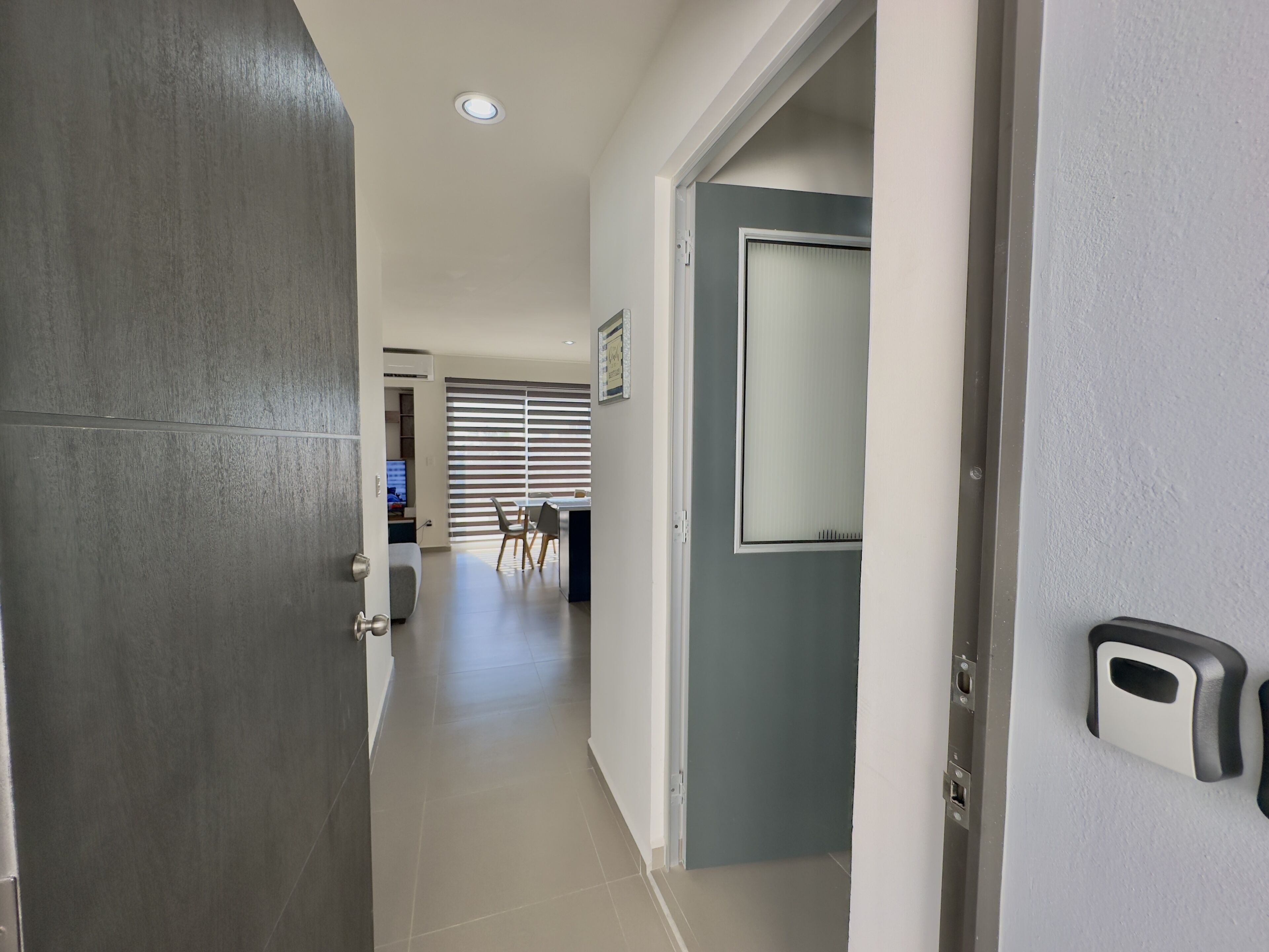 Un pasillo con una puerta gris, una puerta blanca y un interfón mural.