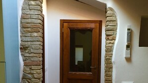 Un pasillo con puerta de madera, pilares de piedra y suelo de baldosas.