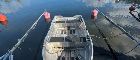 Un pequeño bote amarrado a un muelle de madera, con un lago tranquilo y árboles al fondo.