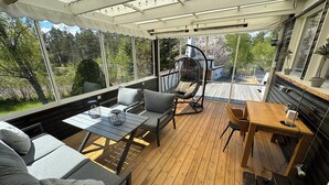 Un espacio de estar al aire libre cubierto con cubierta de madera, asientos acolchados y una silla colgante.