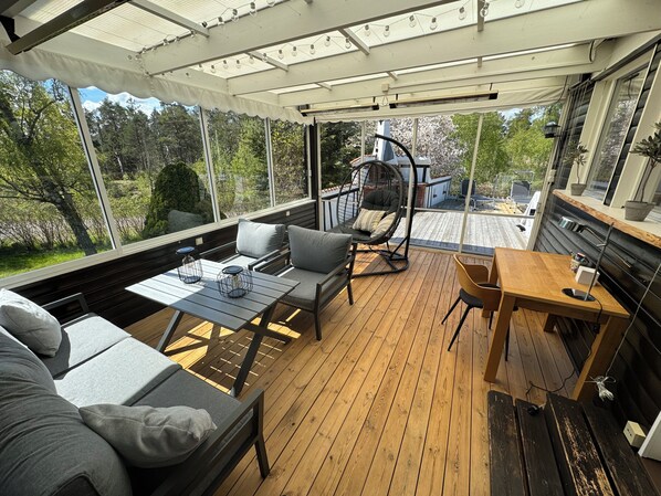 Un espace extérieur abrité, doté d’une terrasse en bois, de sièges rembourrés et d’un fauteuil suspendu.