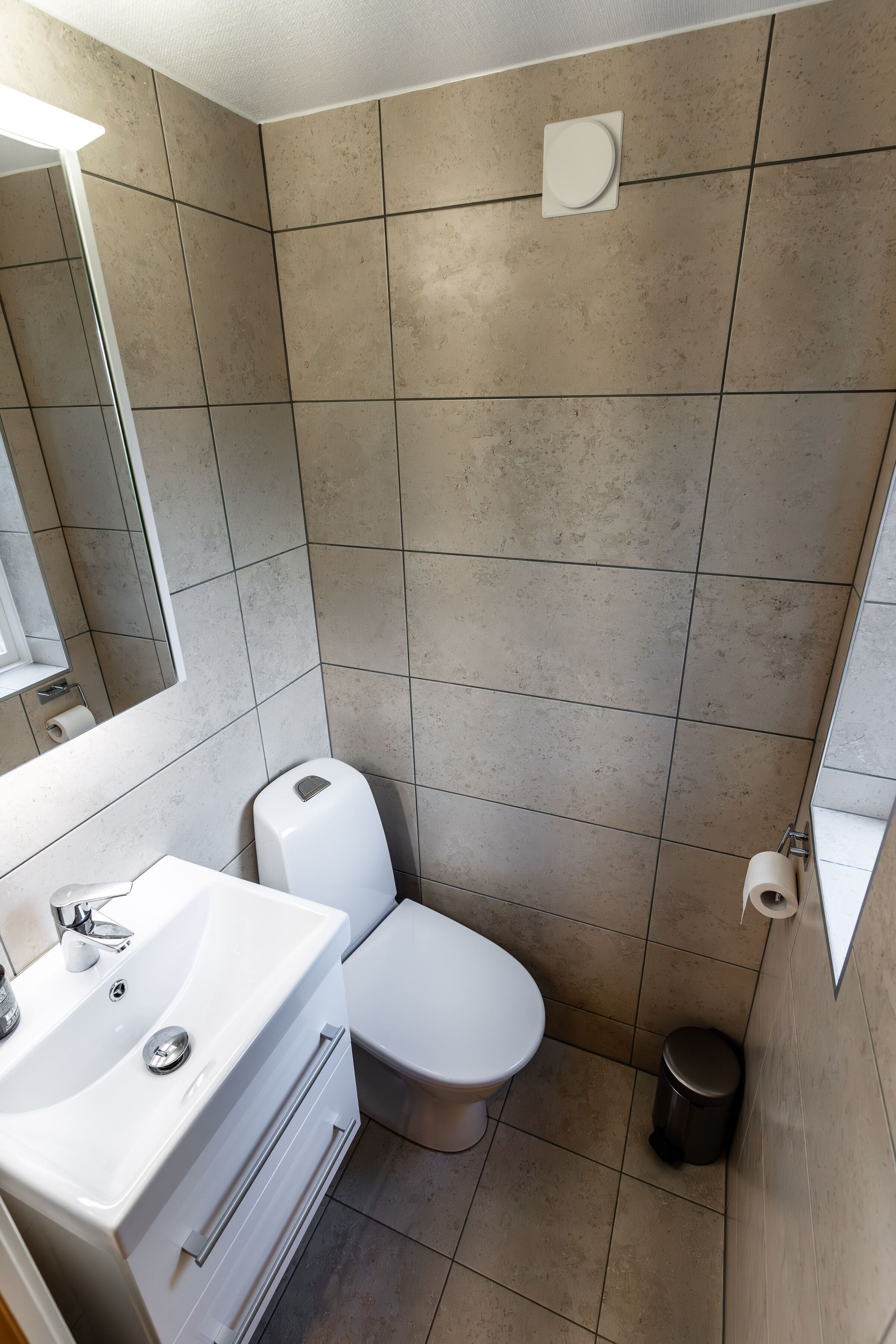 Une petite salle de bain moderne avec un lavabo, des toilettes et un miroir, le tout de couleur blanche.