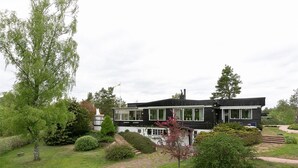 Una casa moderna de dos pisos con fachada blanco y negro, rodeada por un jardín cuidado con diversos arbustos y césped.