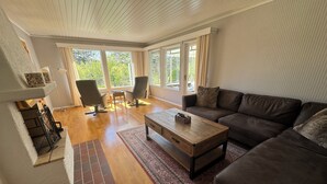 Una sala de estar moderna con piso de madera, un sofá de cuero marrón, dos sillones, una mesita de centro y una chimenea.