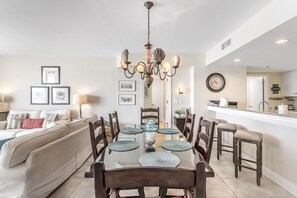 Un coin repas avec une table à plateau de verre, entourée de chaises en bois, et un lustre au-dessus.