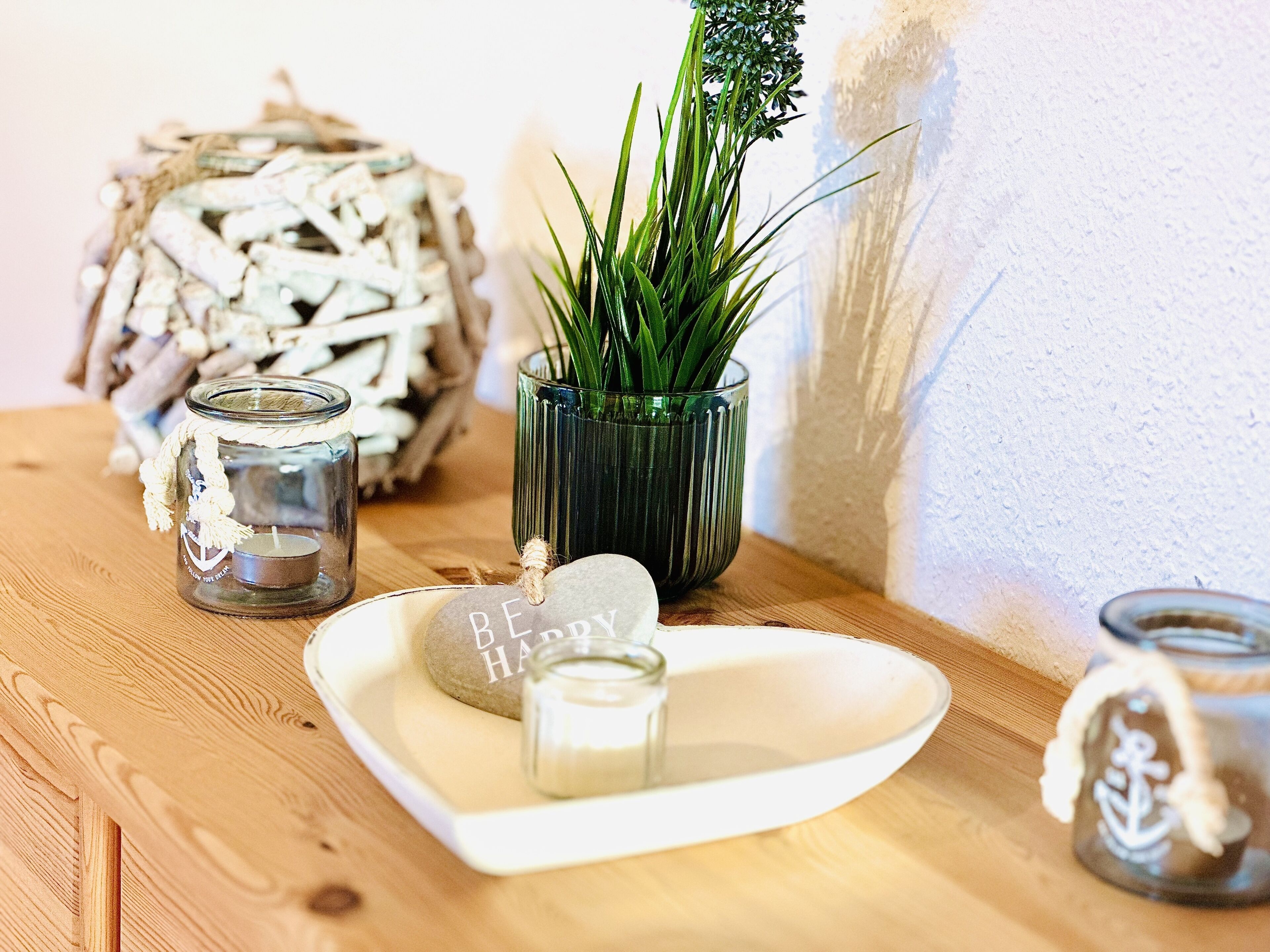 Una mesa de madera con un candelabro de vidrio, una planta en maceta, una piedra decorativa y un frasco de vidrio con un diseño de ancla.