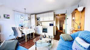 Un espace de vie compact comprenant un coin repas, une kitchenette et un canapé avec une table basse en verre.