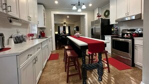 A modern kitchen with white cabinets, a central island with a red tablecloth, and a stainless steel refrigerator.