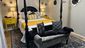 A four-poster bed with a canopy, a nightstand with a lamp, decorative wall art, and a patterned rug.