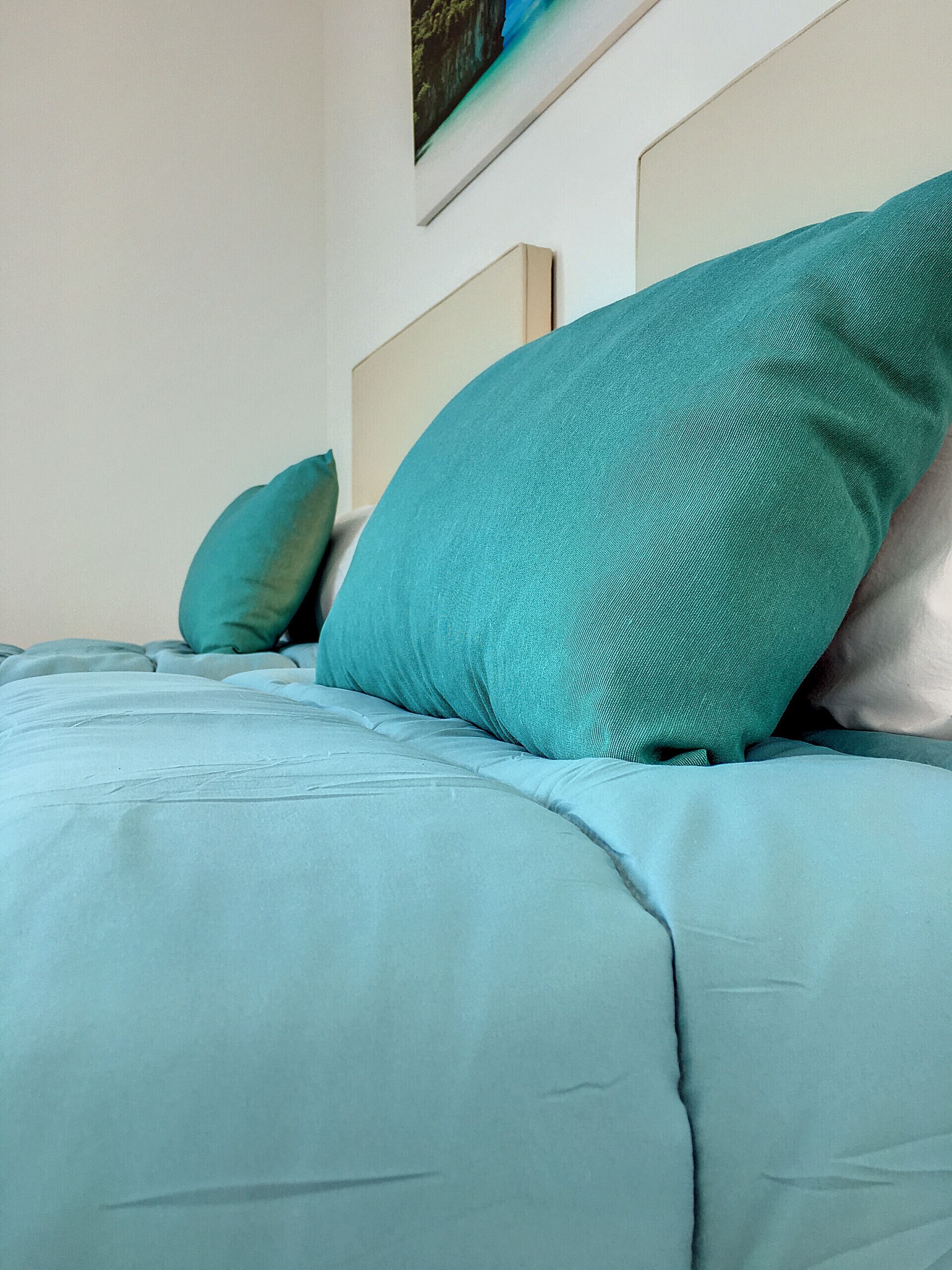 A bed with teal bedding and pillows, a headboard, and a framed picture on the wall.