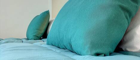 A bed with teal bedding and pillows, a headboard, and a framed picture on the wall.