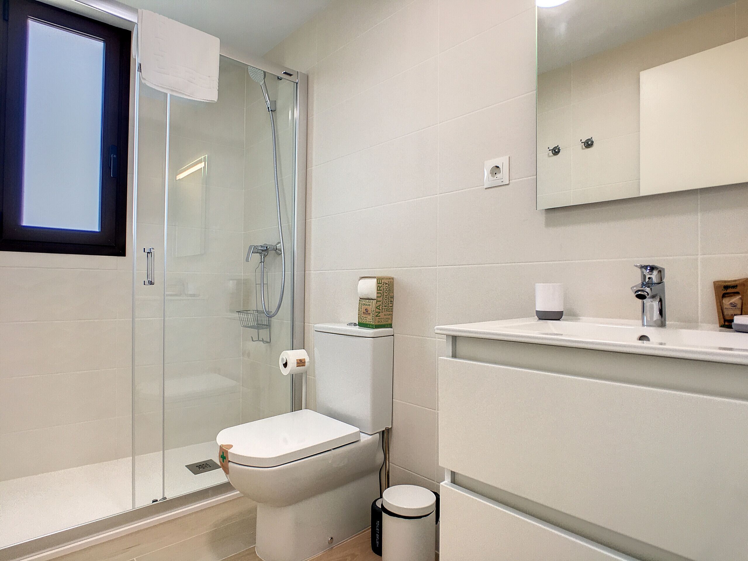 A modern bathroom with a glass-enclosed shower, a toilet, and a sink with a mirror above.